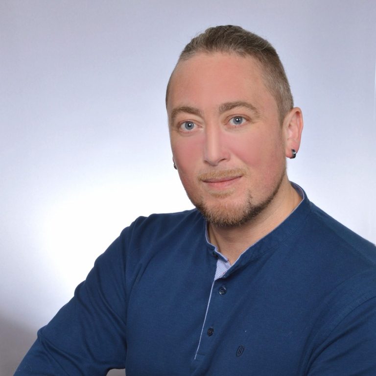 Chris, wearing a blue sweater, looks confidently at the camera.